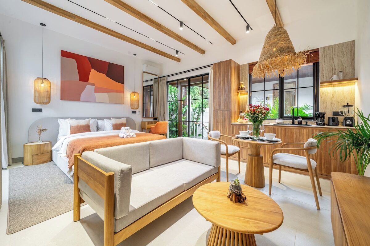 A modern hotel room with a large bed, a sofa, a dining area, and a kitchen.