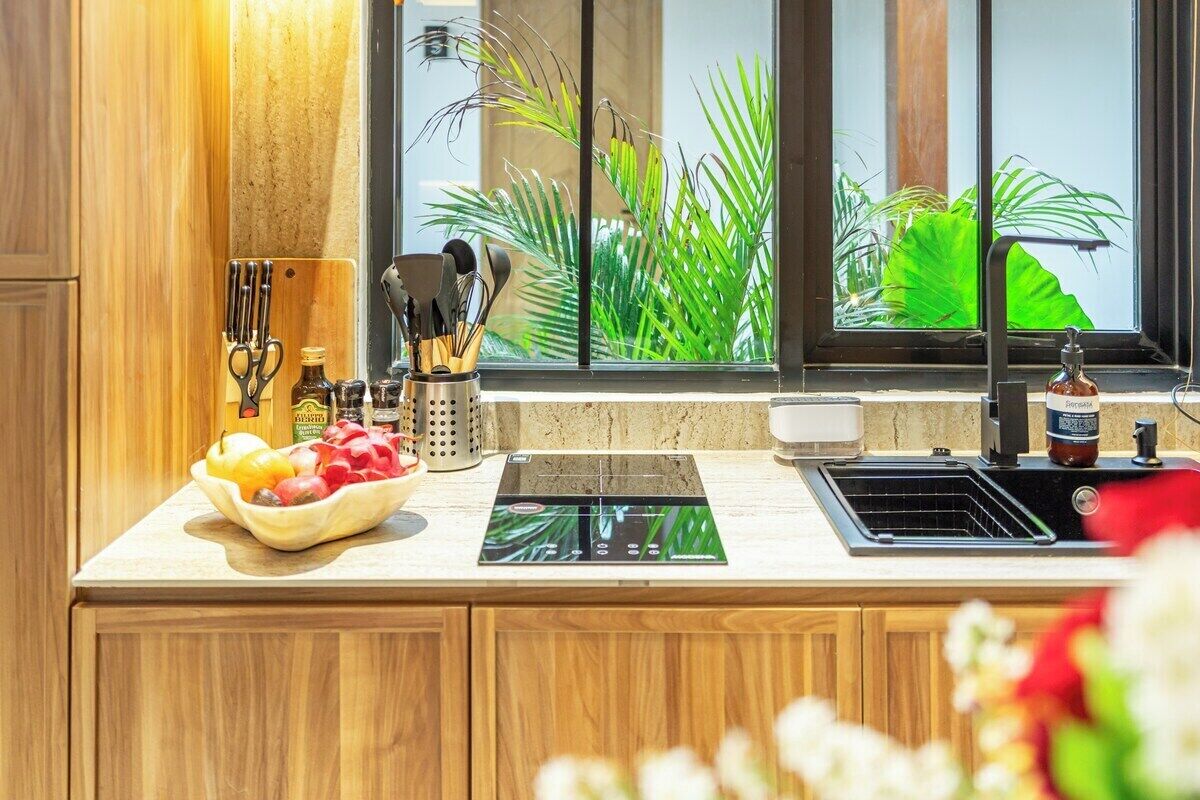 A kitchen with a built-in stove, a sink, and a window with a view of greenery.