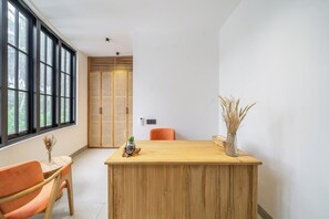 Een kamer met een houten receptiebalie, een stoel, een raam met zonwering en een deur met een geweven patroon.