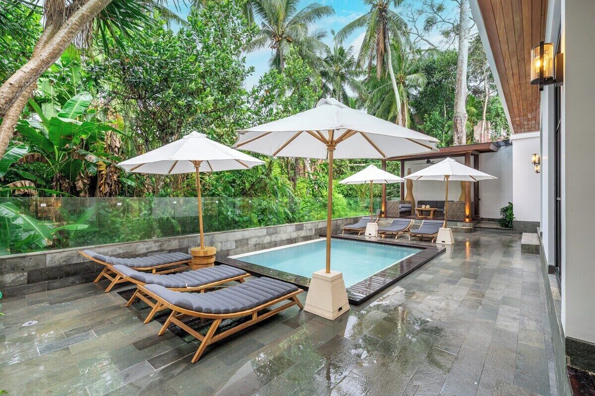 A pool area with lounge chairs and umbrellas, surrounded by lush greenery.