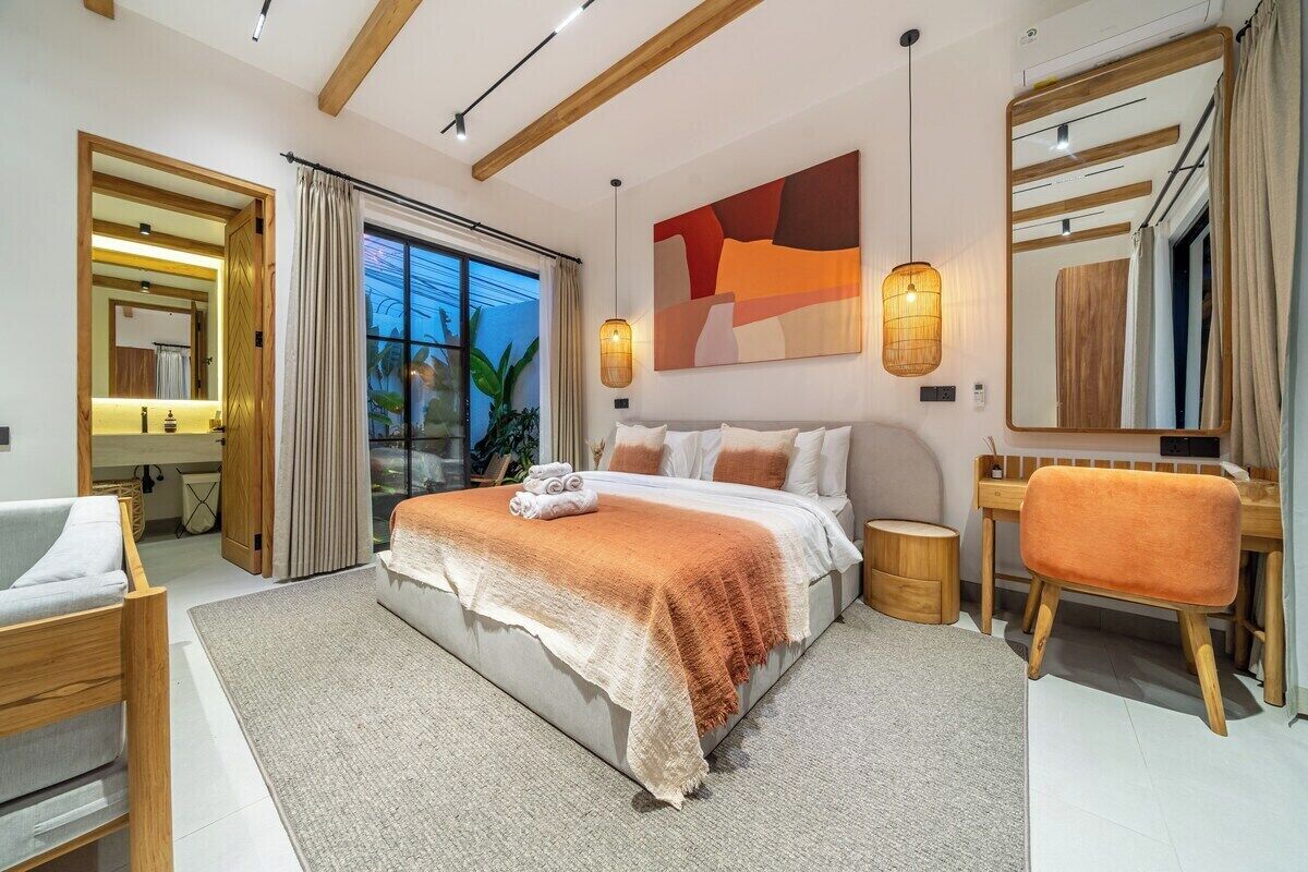 A modern bedroom with a large bed, bedside tables, a chair, a desk, and a large window.