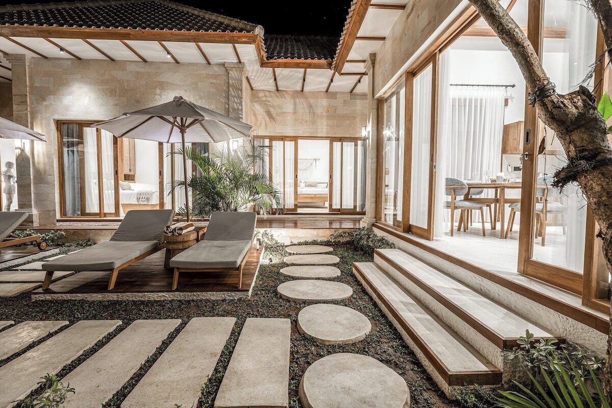 Een modern terras buiten met lounge stoelen, een houten pergola en een geplaveid pad.