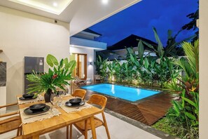 Un espace piscine intérieure aménagé avec un coin repas, le tout entouré de plantes tropicales.