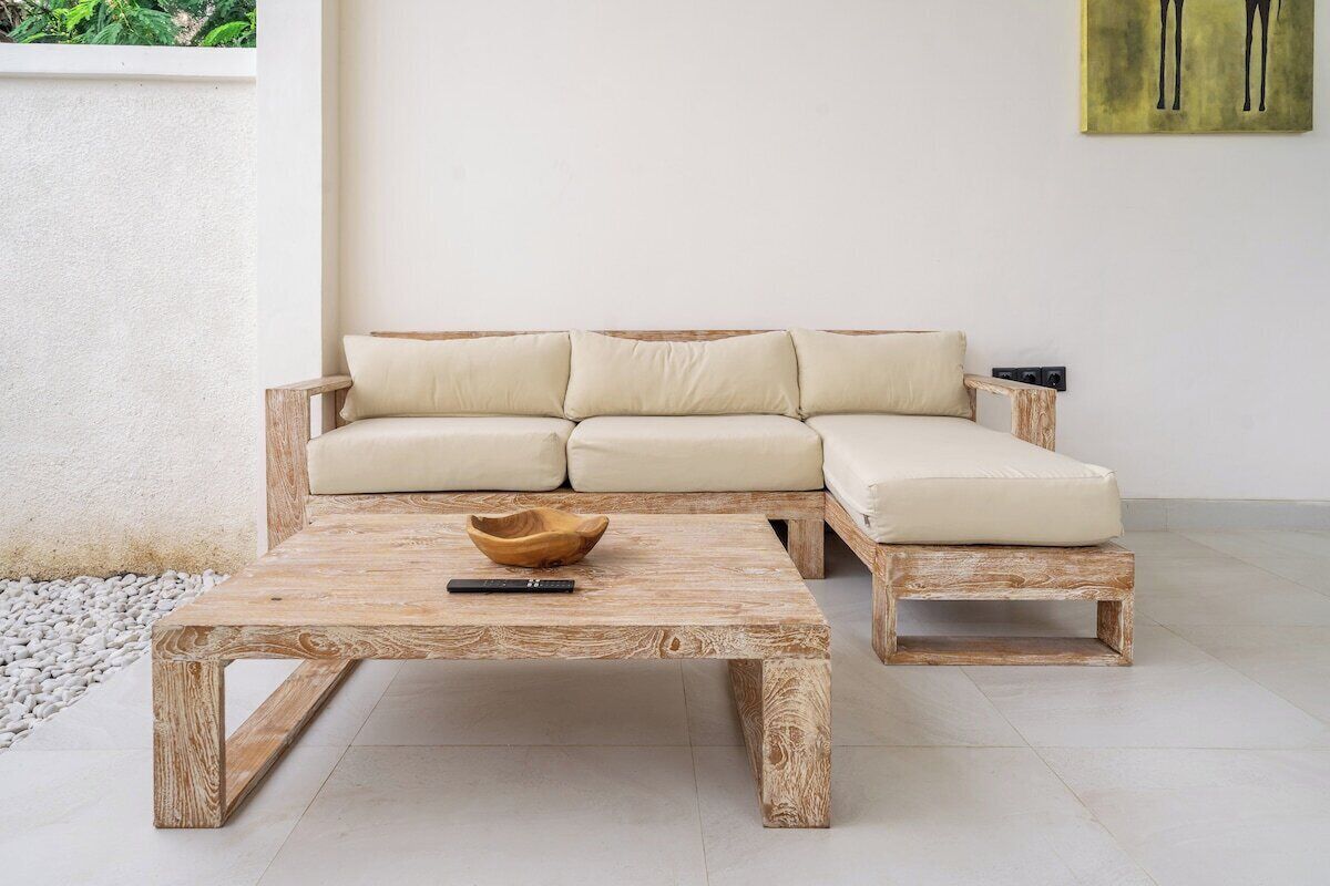 Een houten salontafel met een schaal en een afstandsbediening, een beige bank met kussens en een schilderij aan de muur.