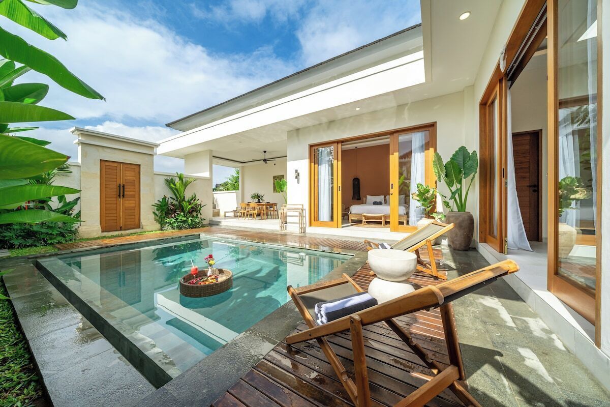 Una casa moderna con piscina, mobiliario exterior y un amplio ventanal corredera que da a un dormitorio.