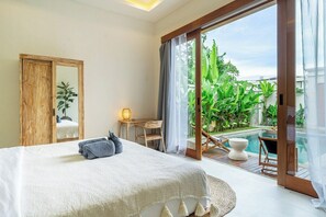 Une chambre dotée d’un grand lit, d’une armoire en bois, d’un bureau avec une chaise, et offrant une vue sur une piscine et un espace verdoyant.