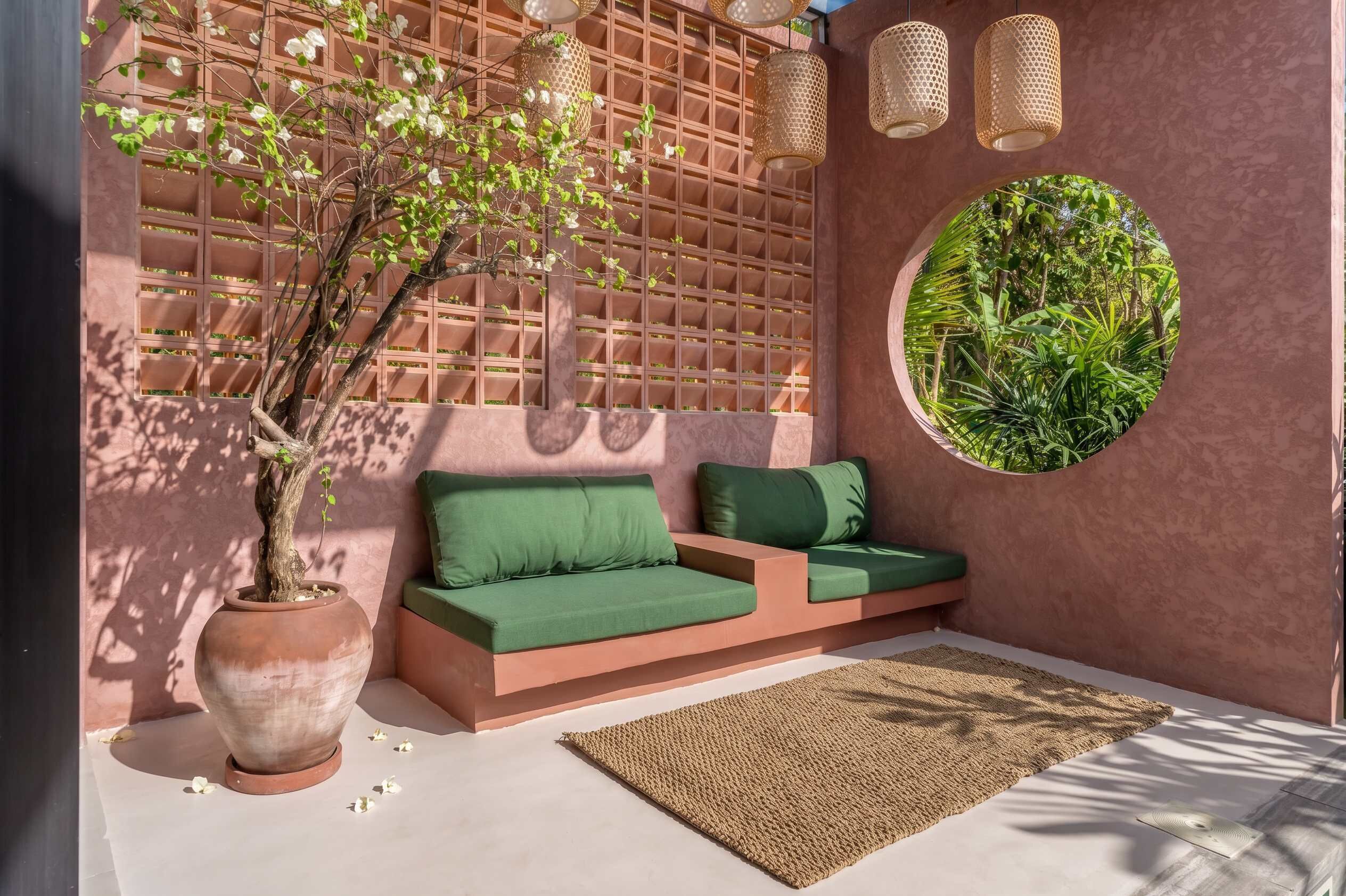 Un espace extérieur moderne, aménagé avec un canapé, un grand bac à plantes et une fenêtre circulaire ornée de verdure.