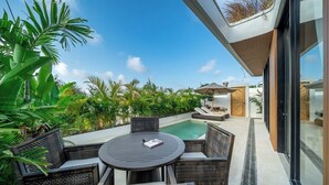Ein moderner Außenbereich mit Sitzgelegenheit, einem runden Tisch, Stühlen, einem Pool und üppiger Bepflanzung.