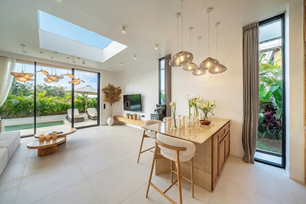 Una cocina moderna con una isla grande, luces colgantes y vistas al exterior con zonas verdes.