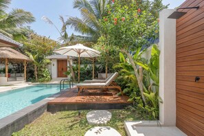 A pool area with a wooden deck, lounge chairs, and a thatched-roof structure. - New Chic 2BR Villa • Huge Pool • Garden Bath+Patio (Gianyar Regency)