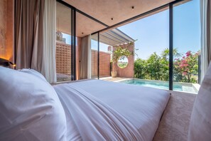 Ein Schlafzimmer mit einem großen Bett, Blick auf einen Swimmingpool und einer Ziegelwand.
