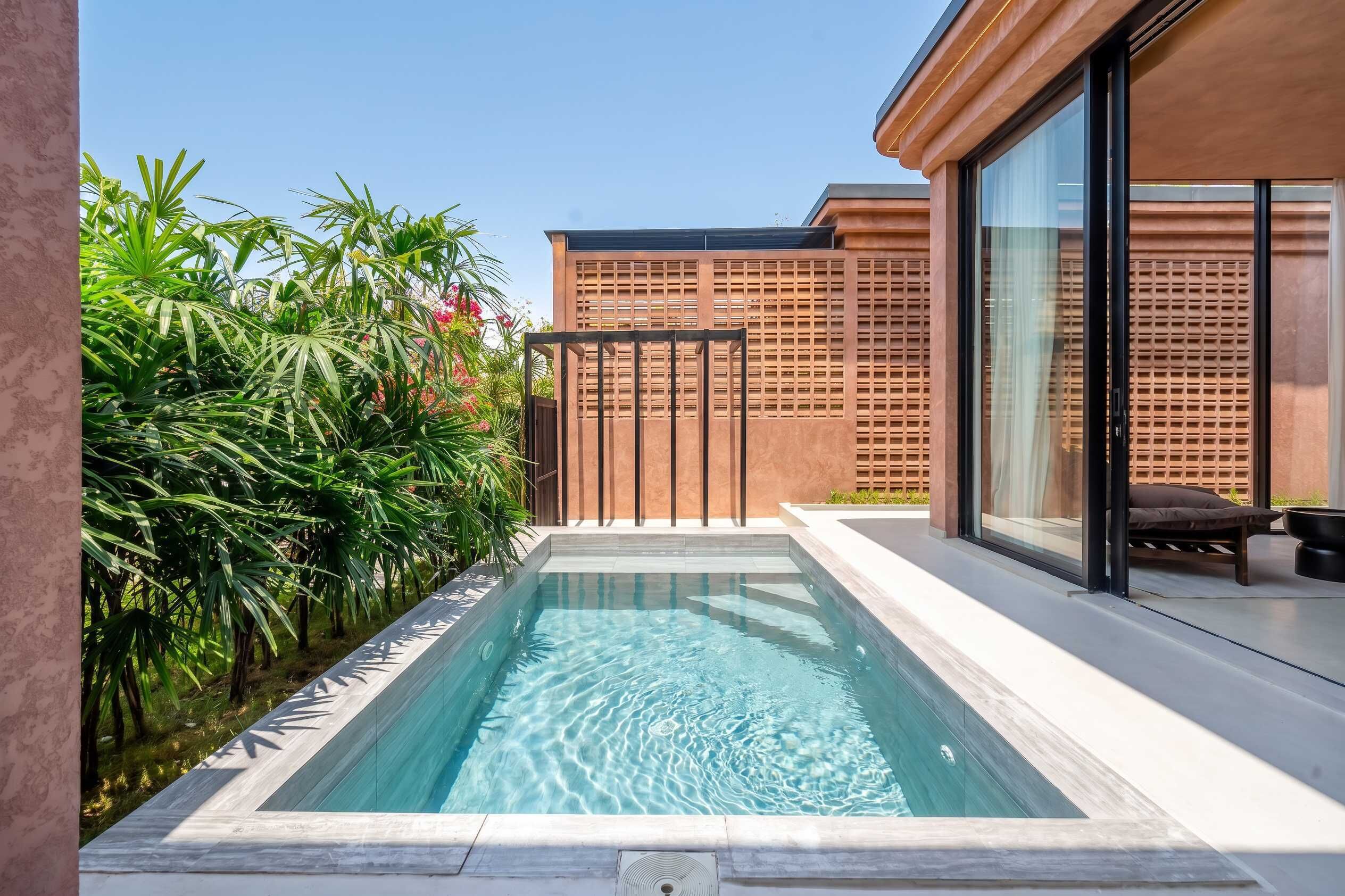 Une piscine moderne à l’eau d’un bleu cristallin, entourée d’une végétation luxuriante et délimitée par une clôture en bois.