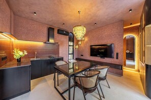 A modern kitchen with a dining area, featuring a chandelier, a flat-screen TV, and a built-in oven. - Tropical 1BR Hideaway in Ungasan w Pool & Patio (South Kuta)