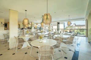 A spacious indoor dining area with round tables and wicker chairs, featuring large windows and hanging rattan lamps. - Aster Apartement 334 - 2-storey Flat w Beach Access, Pool, Gym & Sauna (Kabupaten Badung)