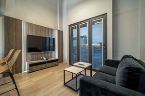 Un salon moderne avec un téléviseur à écran plat, un canapé, une table basse et un fauteuil en osier.