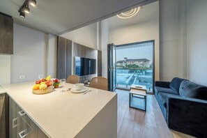 A modern kitchen with a dining area, a sofa, and a view of a building through a large window. - Aster Apartement 334 - 2-storey Flat w Beach Access, Pool, Gym & Sauna (Kabupaten Badung)