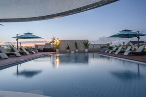 Ein Poolbereich mit Liegestühlen und Sonnenschirmen, bewölkter Himmel und ein Sonnenuntergang.