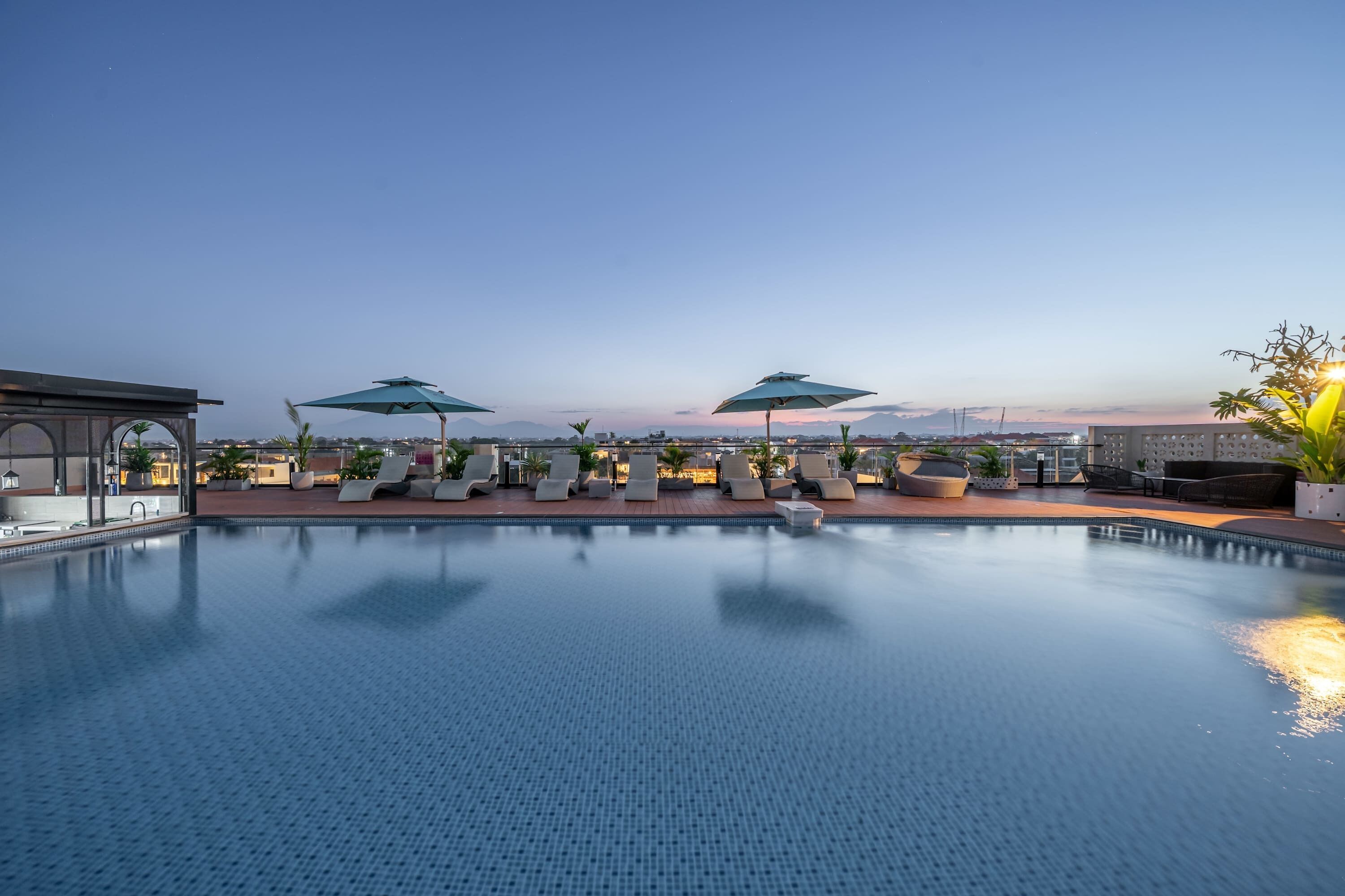 A rooftop pool with lounge chairs and umbrellas, surrounded by a cityscape.
