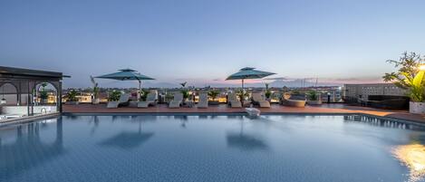 A rooftop pool with lounge chairs and umbrellas, surrounded by a cityscape.