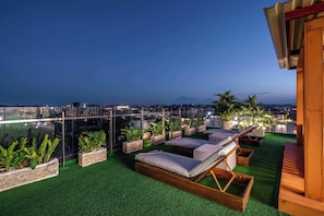 Une terrasse sur le toit, dotée d’un revêtement en gazon synthétique, de chaises longues et de plantes en pot.