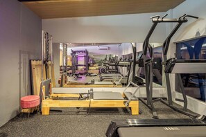 Ein Fitnessraum mit Trainingsgeräten, einer Spiegelwand und einem kleinen roten Hocker.
