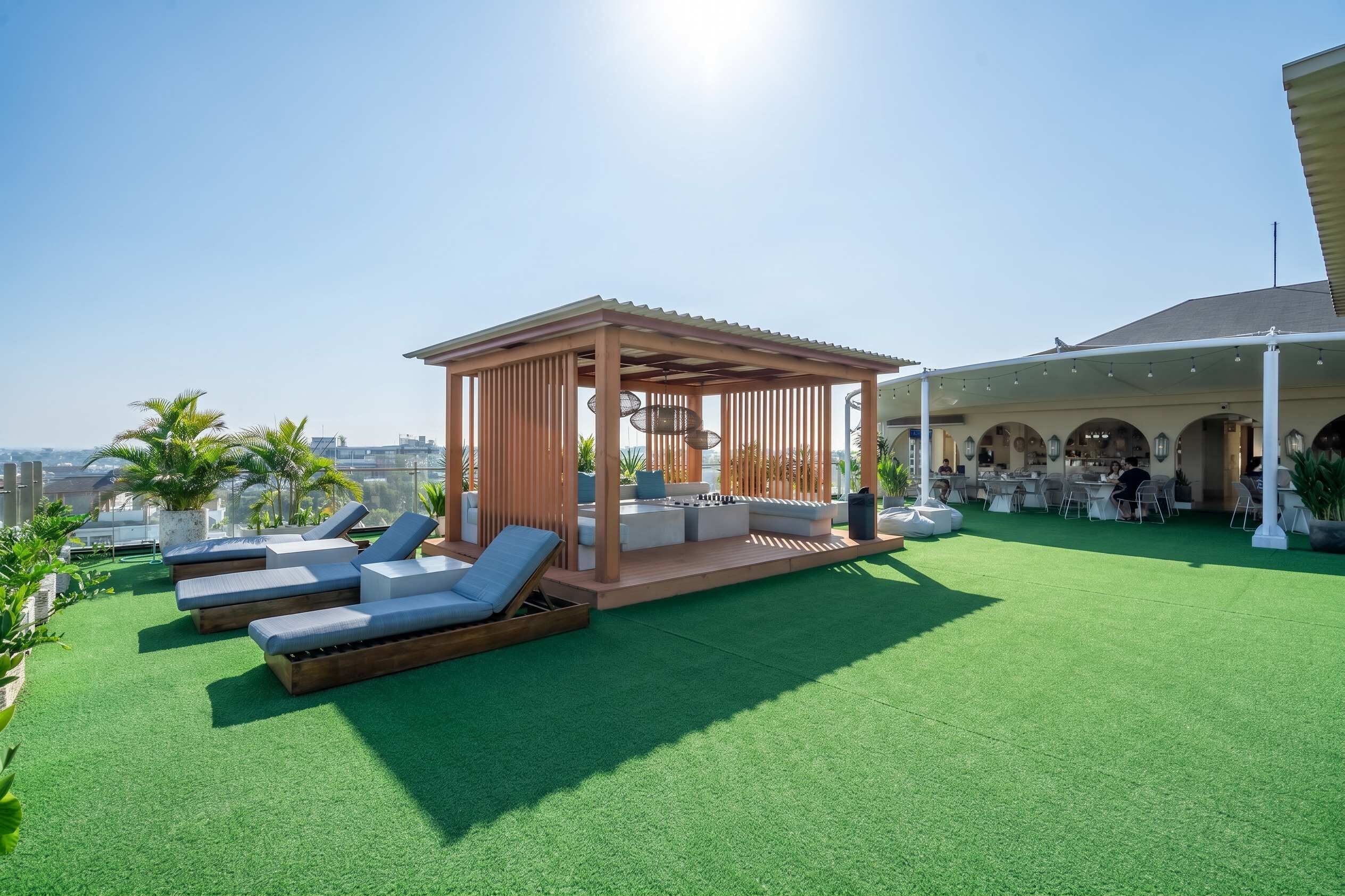 A rooftop terrace with artificial grass, sun loungers, a wooden gazebo, and a covered dining area.