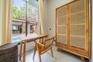 A room with a wooden desk, a wicker chair, and a large wooden wardrobe with a woven front panel. - Cozy 2BR near Canggu's Beaches w Pool & Garden (Kabupaten Badung)