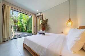 A bedroom with a large bed, a sliding glass door leading to a garden, and a hanging light fixture. - Cozy 2BR near Canggu's Beaches w Pool & Garden (Kabupaten Badung)