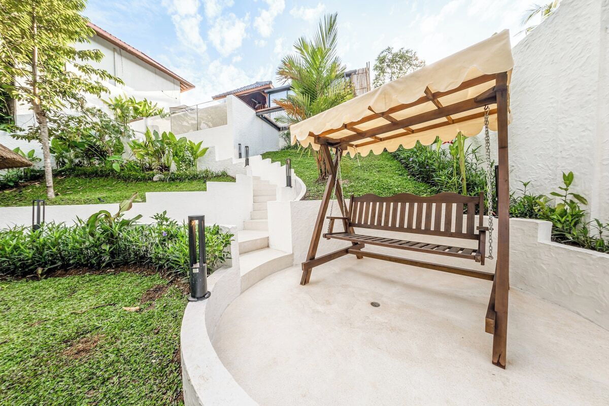 A patio with a wooden swing set, a white wall, and a staircase leading to a building.