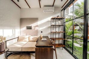 Ein modernes Zimmer mit einer Couch, einem Holztisch, einem Bücherregal und einem großen Fenster mit Blick auf Grünflächen.