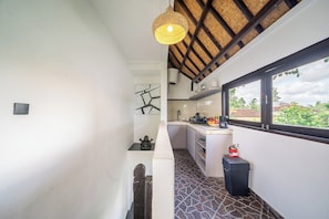 A narrow hallway with a tiled floor, a ceiling with exposed beams, a hanging light fixture, a window with a view of greenery, and a small kitchen area with a sink and countertop. - Cozy 1BR Villa in Lush Ubud w Spa+2 Pools+Balcony (Ubud)