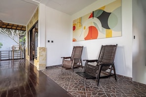 A reception area with a stone floor, two wooden chairs, a large abstract painting, and a view of a balcony with a railing. - Cozy 1BR Villa in Lush Ubud w Spa+2 Pools+Balcony (Ubud)