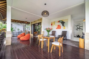 Un espace intérieur comprenant un coin repas avec une table ronde et des chaises, un coin salon avec des fauteuils-pouf orange et un grand tableau abstrait accroché au mur.