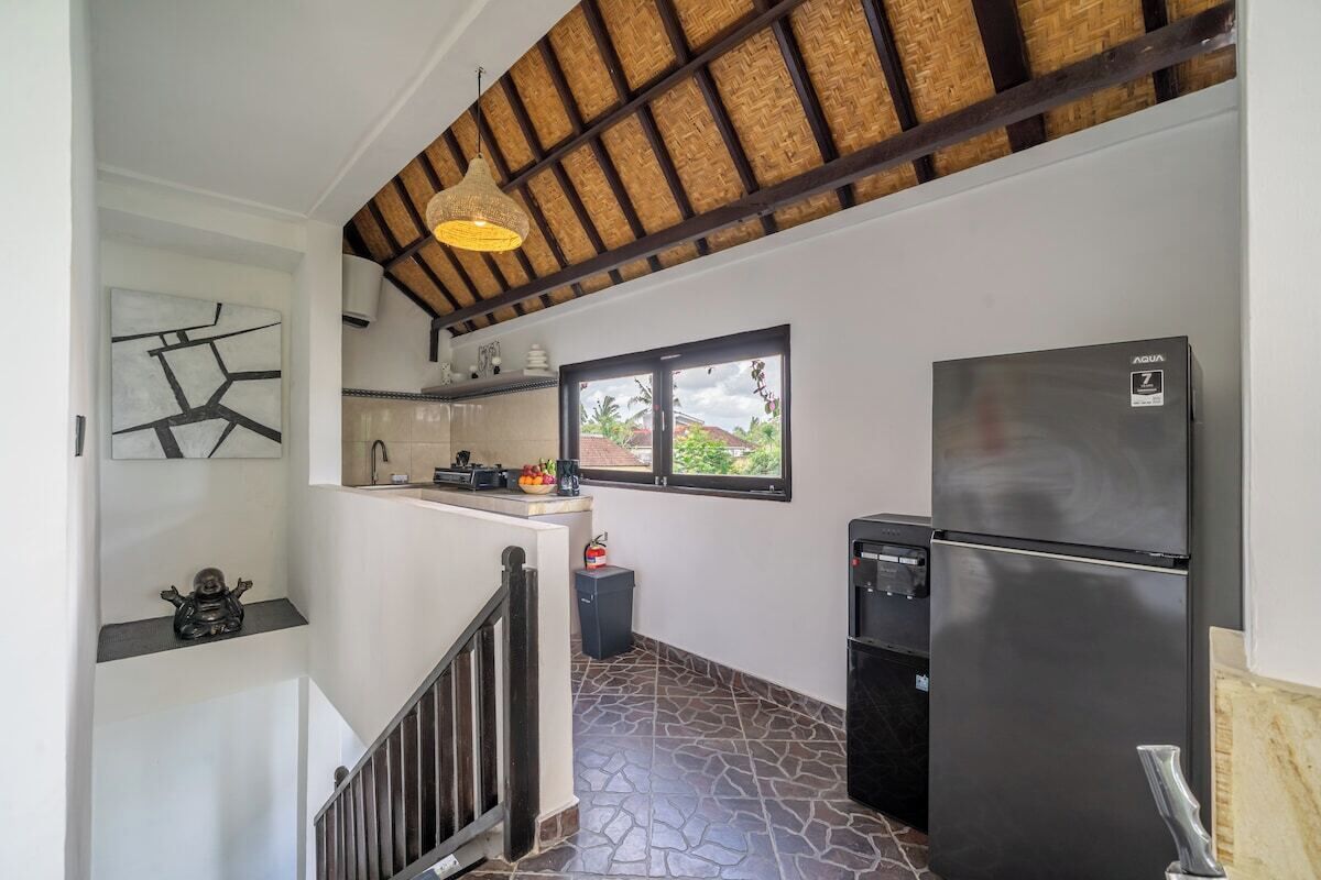 A compact kitchen with a modern refrigerator, a window providing natural light, and a staircase leading to an upper level.