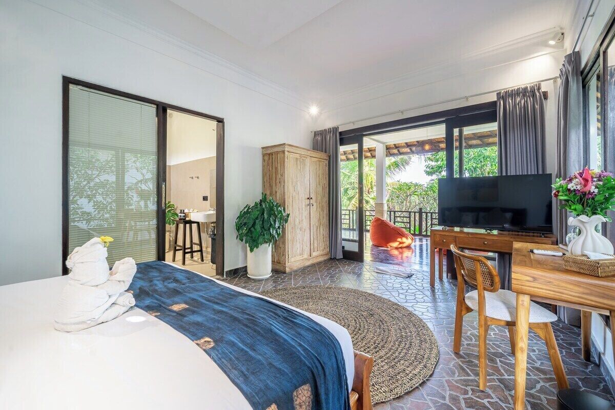 A hotel room with a bed, a desk with a television, a chair, and a view of the outdoors.