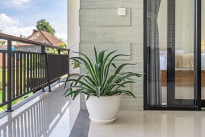 A potted plant on a balcony with a railing, a glass door, and a view of a building in the background. - New Luxury Villa with Jungle Views & Pool in Ubud! (Gianyar Regency)