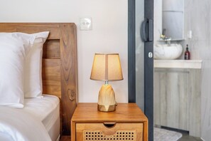 A bed with white bedding, a wooden nightstand with a lamp, and a bathroom in the background. - New Luxury Villa with Jungle Views & Pool in Ubud! (Gianyar Regency)
