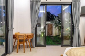 Ein Zimmer mit einer Schiebetür zu einem Garten, einem Holztisch mit Stühlen und einem Bett mit weißer Bettdecke.