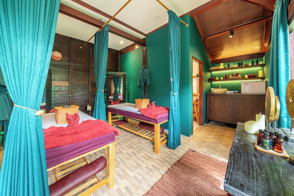 Ein Zimmer mit zwei Betten, einer Massageliege, einem Spiegel und einem Regal mit Flaschen.