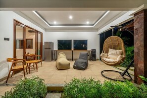 A modern living area with a dining set, two bean bags, a hanging chair, and a kitchen in the background. - PROMO NEW 1 BR in Serene Ubud • Pool, Garden&Patio (Gianyar Regency)