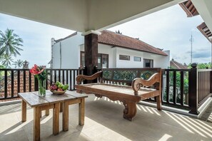 A wooden bench and table on a balcony with a view of a white building and palm trees. - PROMO NEW 1 BR in Serene Ubud • Pool, Garden&Patio (Gianyar Regency)