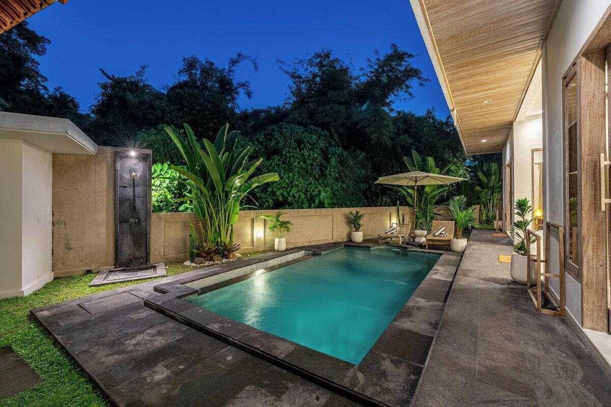 Une piscine dotée d’une terrasse en bois, entourée de plantes en pot et bordée d’un mur en béton.