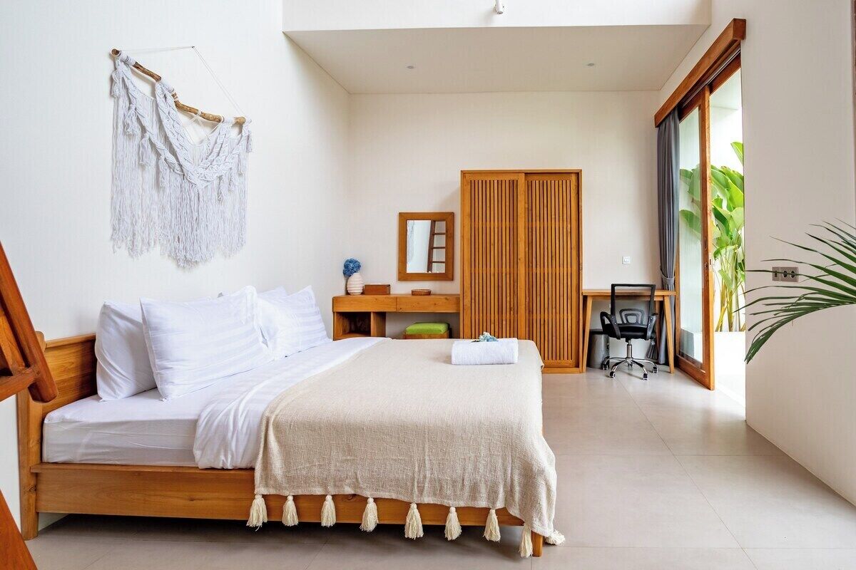 Ein Schlafzimmer mit einem hölzernen Bett, einem Schreibtisch, einem Stuhl, einem Kleiderschrank und einer Wandaufhängung aus Makramee.