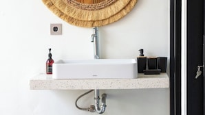 Une salle de bain avec un miroir rond en fibres tressées, un lavabo blanc et deux paniers en fibres tressées.