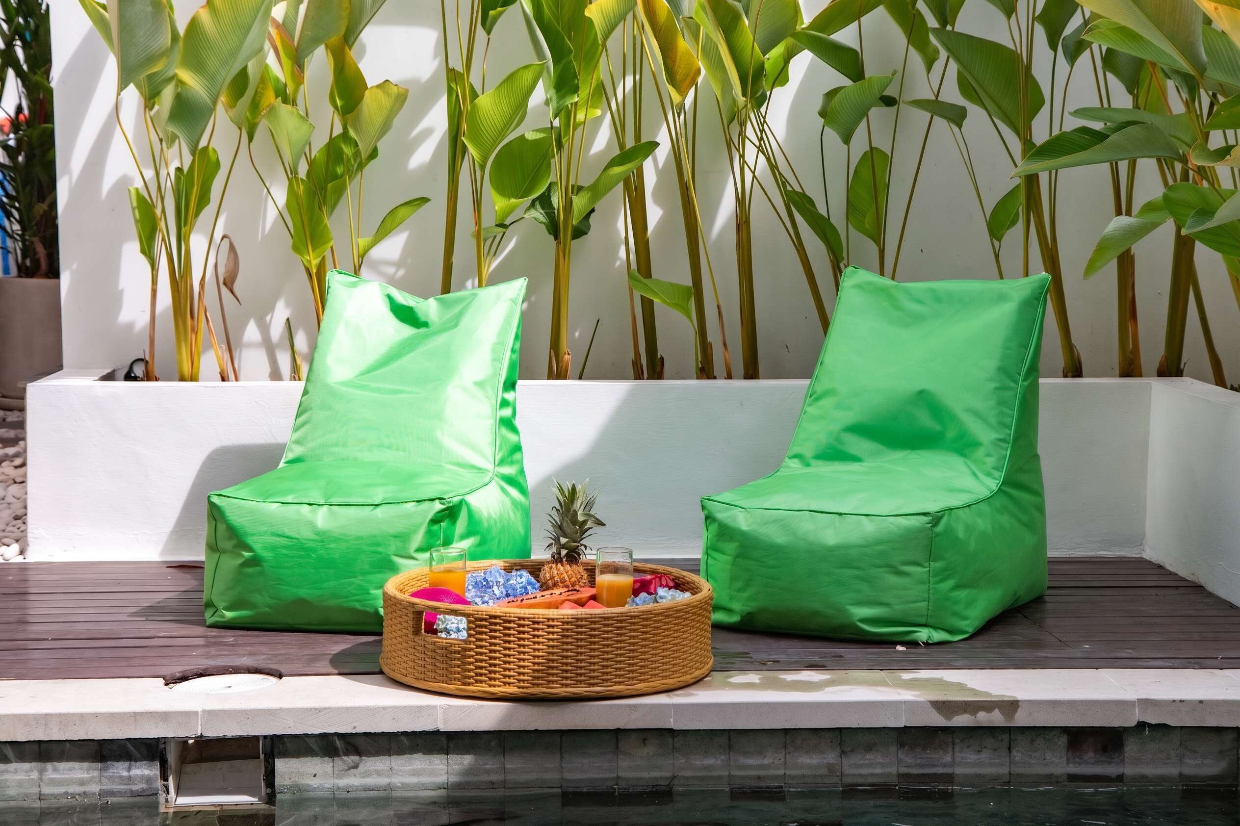 Uma área de estar com dois travesseiros verdes e uma cesta de vime com frutas e bebidas.