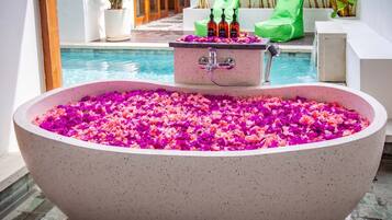 Eine große Badewanne voller Blütenblätter, ein kleines Waschbecken mit Flaschen und ein Pool im Hintergrund.