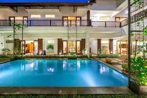 Hotel com vários níveis, piscina central, áreas de estar internas e varanda com guarda-corpo.