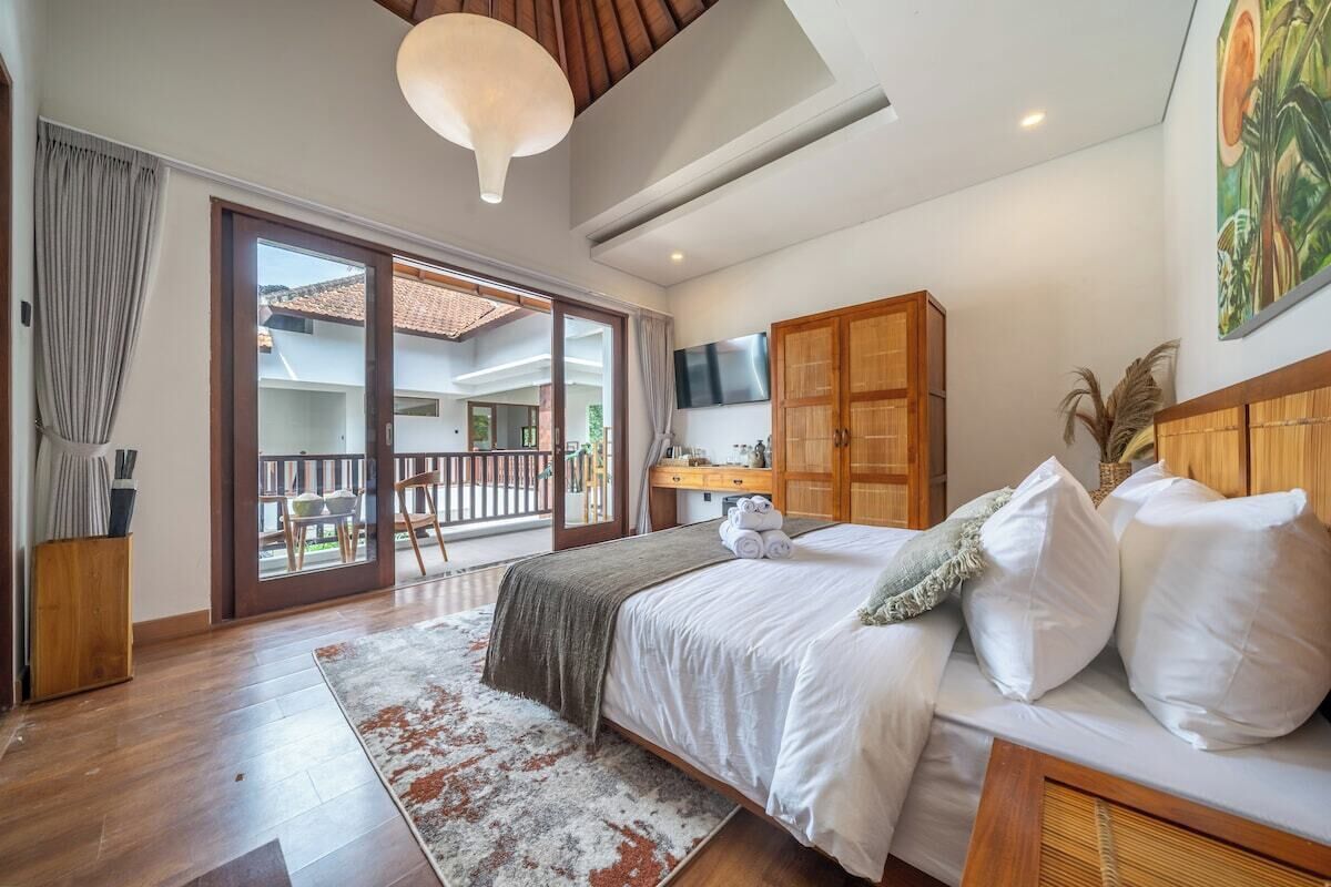 Quarto com cama, guarda-roupa de madeira, televisão e varanda com vista exterior.
