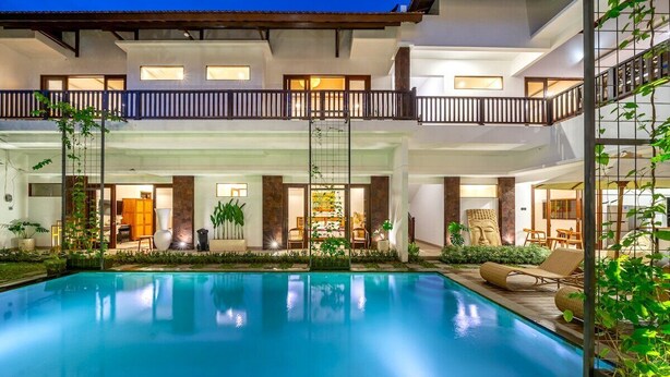 Ein Hotel mit mehreren Etagen, einem zentral gelegenen Schwimmbad, Innenbereichen zum Sitzen und einem Balkon mit Geländer.