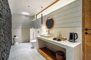 Een moderne badkamer met een witte wastafel, een ronde spiegel en een koffiezetapparaat op het aanrecht.